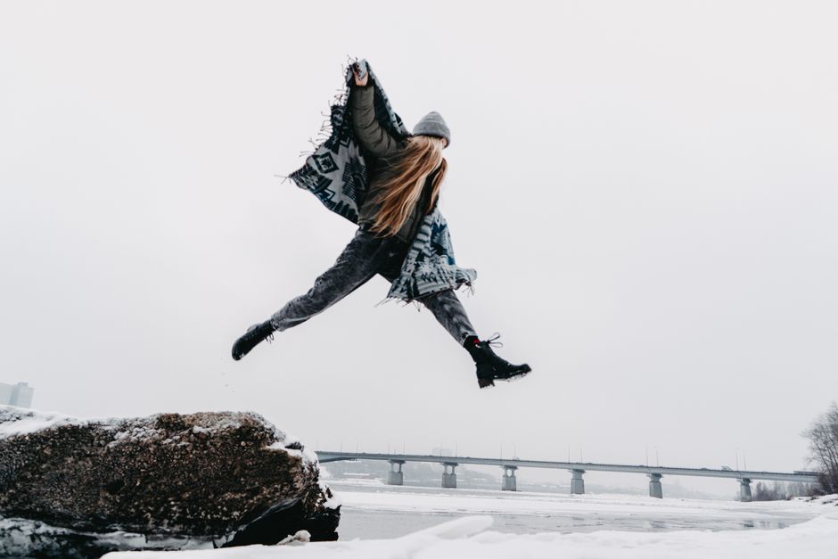 Woman leaping energetically on a snow-covered ground with a bridge in the background.